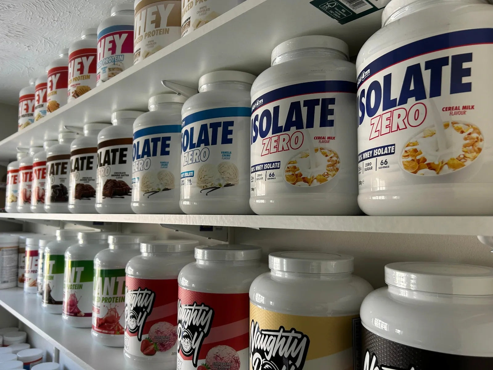 Shelves stocked with various protein powder containers on a white background