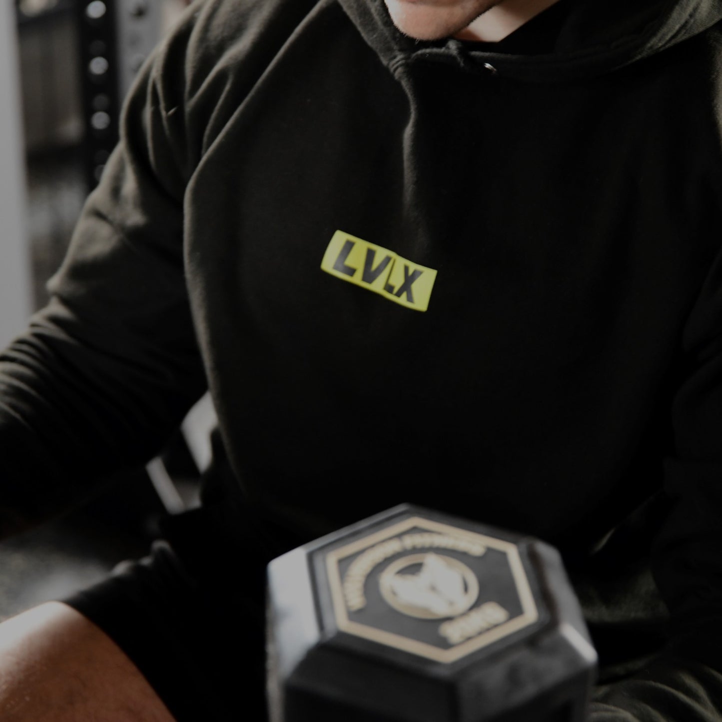 Male model wearing the LVLX hoodie in black, sitting on a bench with dumbbells in hands.