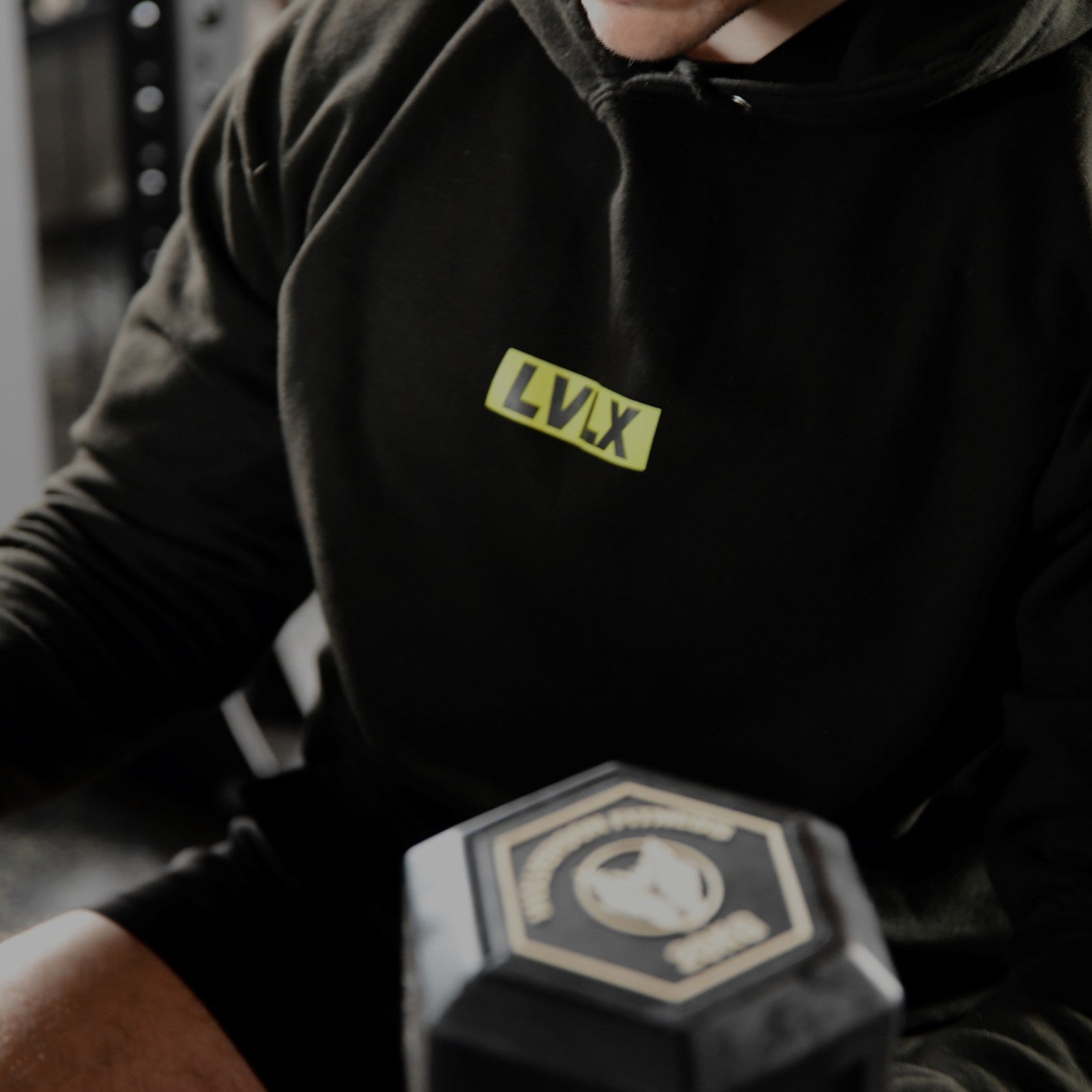 Male model wearing the LVLX hoodie in black, sitting on a bench with dumbbells in hands.
